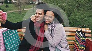 Two cute african american woman taking selfie on smartphone with shopping bags and smiling. Girlfriends sitting on