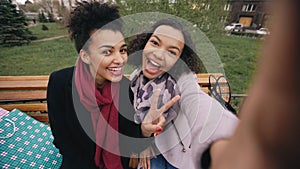 Two cute african american woman taking selfie on smartphone with shopping bags and smiling. Girlfriends sitting on