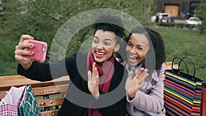 Two cute african american woman taking selfie on smartphone with shopping bags and smiling. Girlfriends sitting on