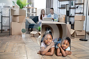 Two cute african girls kids playing in box while parents working on laptop