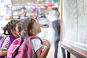 Two cute asian child girls with backpack looking at map