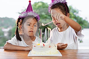 Two asian child girls lighting candle on birthday cake together in birthday party