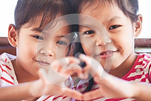 Two cute asian child girls making heart shape with hands together