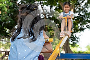 Two cute asian child girls playing seesaw together in the playground