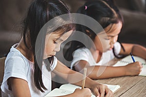 Two cute asian child girls reading a book and writing a notebook in the classroom