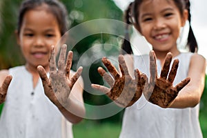 Two cute asian child girls showing dirty hands after planting the tree together