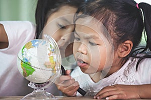 Two cute asian child girls use magnifier to look and study at the globe in classroom