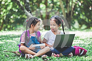 Two cute asian child girls using laptop in the park together