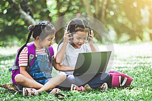 Two cute asian child girls using laptop in the park together