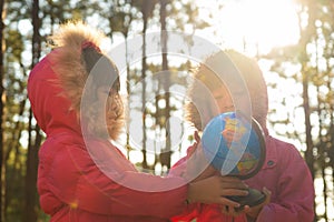 Two cute Asian girls learning a model of the world on nature background and warm sunlight in the park. Children learn through