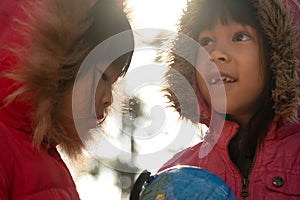 Two cute Asian girls learning a model of the world on nature background and warm sunlight in the park. Children learn through