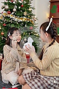 Two cute Asian girls are opening their Christmas gifts, playing toys in the living room together