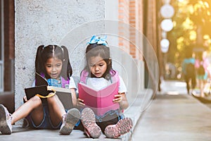 Two cute asian pupil girls reading a book  together in the school with fun and happiness