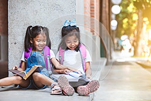 Two cute asian pupil girls reading a book  together in the school with fun and happiness