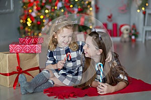 Two cute awesome girls sisters celebrating New Year Christmas close to xmas tree full of toys in stylish dresses with candies