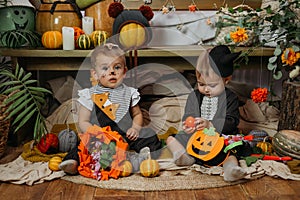 Two cute baby girl dressed in Halloween costume sitting on bed with Halloween decoration at home. Lifestyle indoors