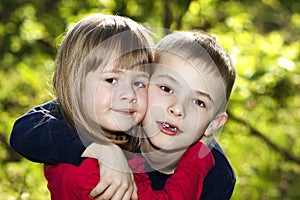 Two cute blond funny happy smiling children siblings, young boy brother embracing sister girl outdoors on bright sunny green bokeh