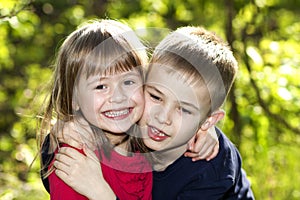 Two cute blond funny happy smiling children siblings, young boy brother embracing sister girl outdoors on bright sunny green bokeh