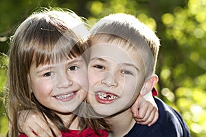 Two cute blond funny happy smiling children siblings, young boy brother embracing sister girl outdoors on bright sunny green bokeh