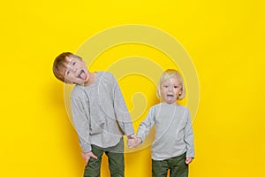 Two cute boys have fun and show their tongues. Studio photography on a colored yellow background.