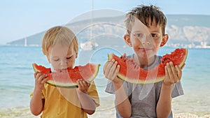 Two cute boys savoring sweet watermelon on a sea beach towel. Spirit of summertime, holiday delights, vacation happiness