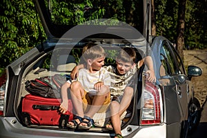 Two cute boys sitting in a car trunk before going on vacations with their parents. Two kids looking forward for a road