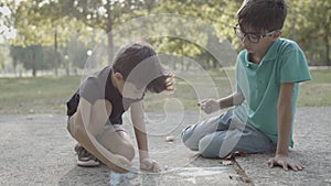 Two cute boys sitting on ground and drawing with chalks