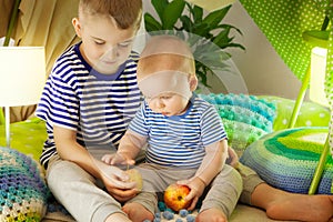 Two cute brothers eat apples in a children`s tent. 6 years old boy and baby toddler