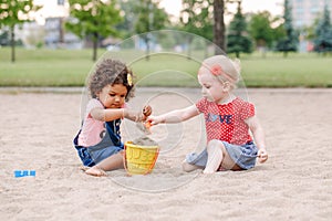 Two cute Caucasian and hispanic latin toddlers babies children sitting in sandbox playing with plastic colorful toys