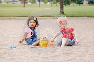 Two cute Caucasian and hispanic latin toddlers babies children sitting in sandbox playing with plastic colorful toys