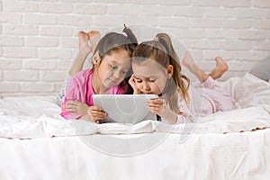 Two cute children girls use digital tablet in bed.