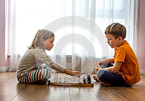 Two cute children playing chess at home or kindergarten. Table game. Preschool boy and girl play on the floor with