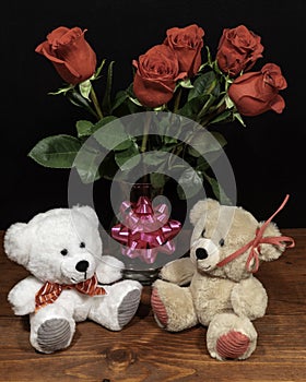 Two cute cuddly teddy bears with red roses in vase and pink bow on wooden table on dark background