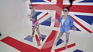 Two cute females in sunglasses workout synchronic dancing in studio with UK flag