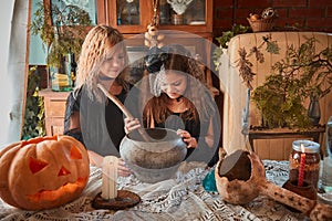 Two cute girls aged 10 years in witch costumes in an old house on Halloween brew a magic potion and conjure.
