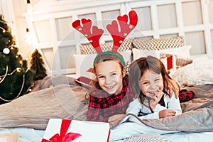 Two cute girls with Christmas presents, playing on the bed