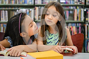 Two cute girls are jealous of each other while reading books in library while teacher teaching. People lifestyles and education.