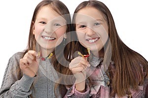 Two cute girls playfully pose with orthodontic appliances in their hands on a white background. The concept of oral hygiene in
