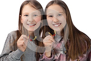 Two cute girls playfully pose with orthodontic appliances in their hands on a white background. The concept of oral hygiene in