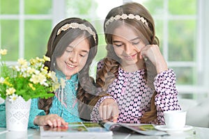 Portrait of two cute girls reading magazine