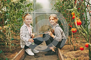 Two cute girls with a tablet in their hands examine a sample of a plant through a magnifying glass. Curious children