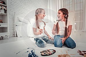 Two cute girls in white tshirt and jeans painting sitting on bedroom floor