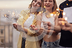 Two cute guys and two charming girls are holding sparklers and smiling