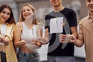 Two cute guys and two charming girls are holding sparklers and smiling