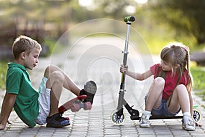 Two cute happy funny laughing young children, brother and sister, having fun on sunny pavement, handsome boy with skateboard and