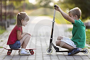 Two cute happy funny smiling young children, brother and sister, posing for camera, handsome boy with scooter and pretty long-