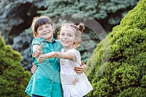 Two cute happy girls playing outdoors. Kids having fun in summer park. Friends standing near green trees