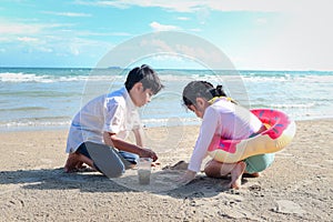 Two cute kids boy and girl having fun together on sandy summer beach with blue sea, happy childhood friend playing with sand on