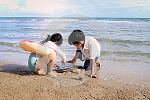 Two cute kids boy and girl having fun together on sandy summer beach with blue sea, happy childhood friend playing with sand on