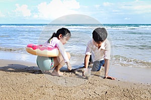 Two cute kids boy and girl having fun together on sandy summer beach with blue sea, happy childhood friend playing with sand on